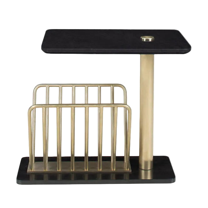 A modern side table with a black rectangular top and base, a central gold metal pedestal, and a gold wire magazine rack on a white background.