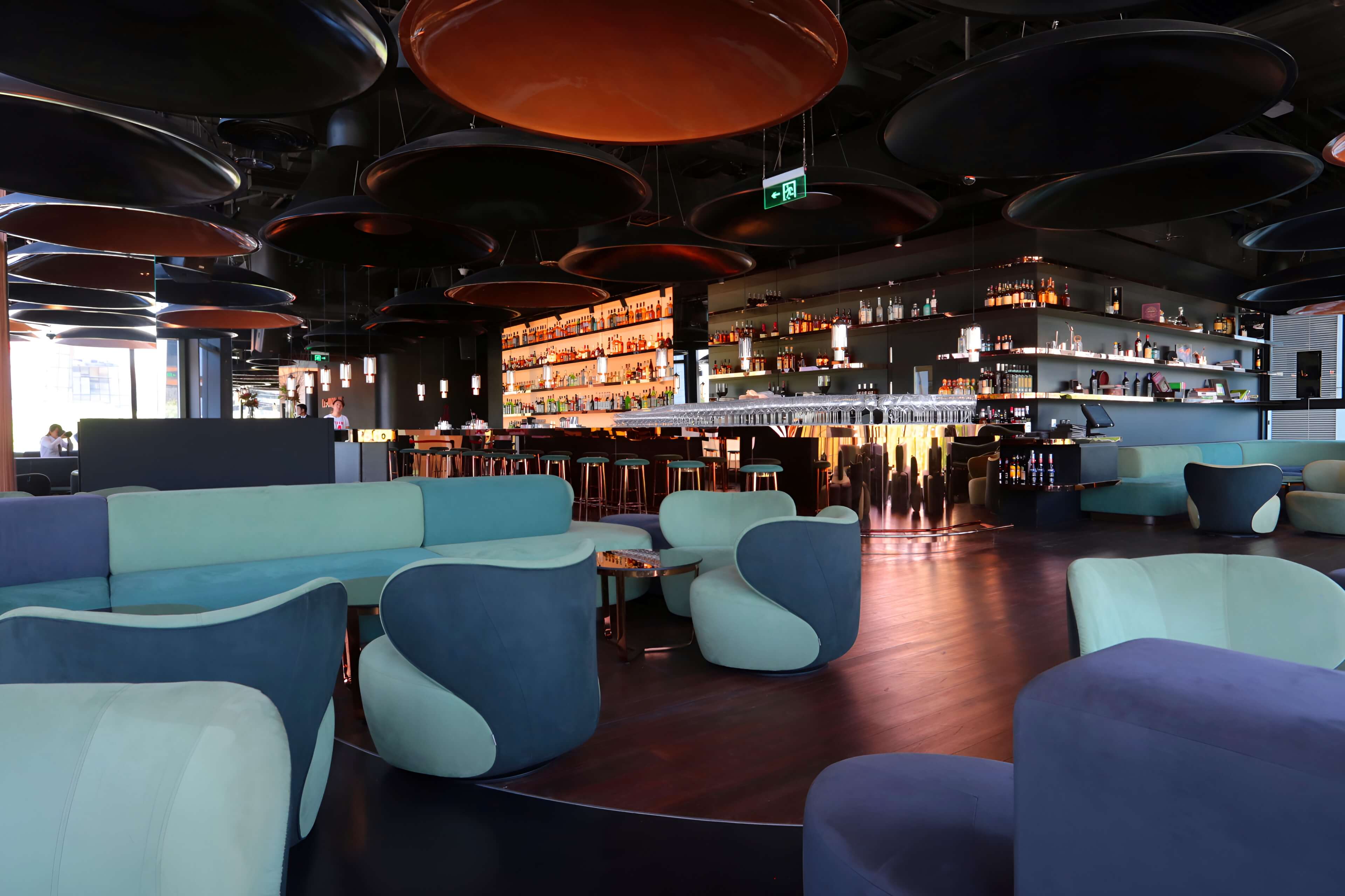 Modern lounge with blue and green furniture and a bar in the background.