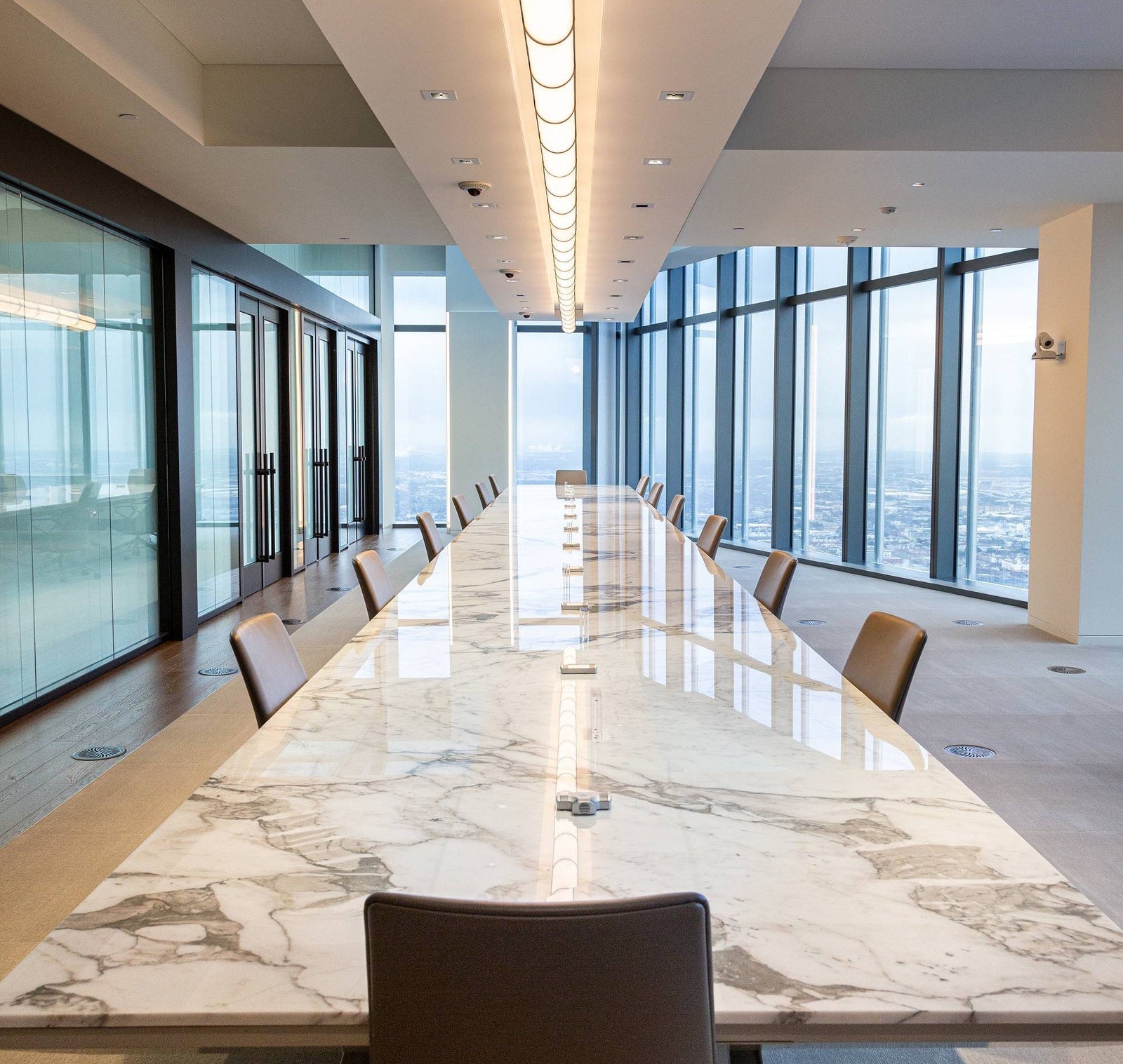 Modern conference room with a long marble table and chairs, large windows overlooking a cityscape.