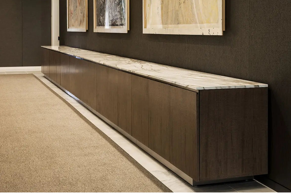 A long modern console cabinet with a dark wood grain finish and a light marble top, positioned against a dark textured wall with framed artwork above.