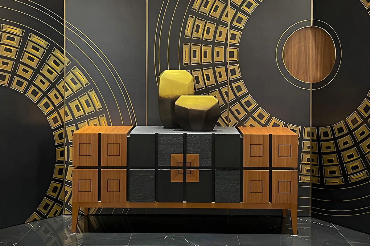 A mid-century modern sideboard cabinet with a geometric design, featuring wood-grain panels, textured black doors, and a central gold accent, styled with two sculptural yellow chairs against a matching black and gold patterned backdrop.