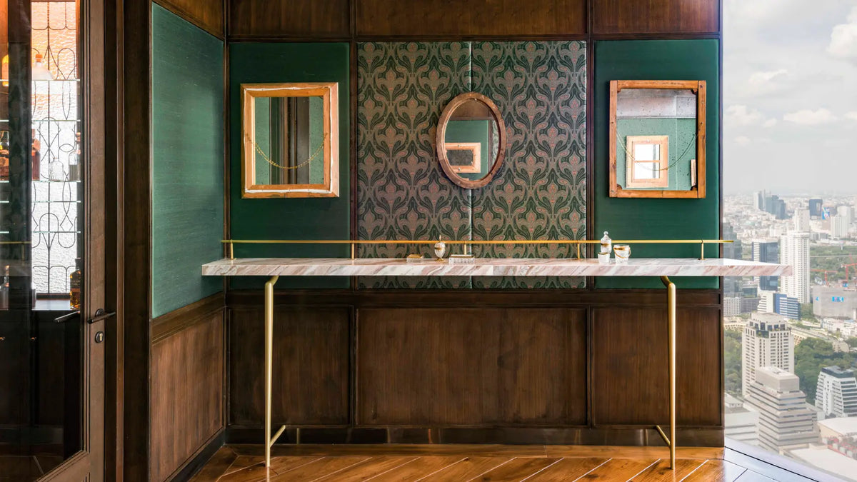 An elegant vanity station with a marble countertop, gold metal legs, and a dark wood cabinet, set against a green and patterned wall with mirrors, overlooking a city skyline.