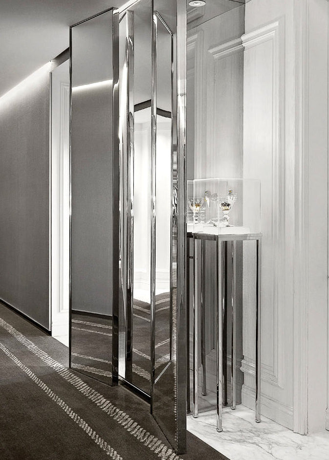 A modern interior hallway with tall mirrored panels, a small marble-top side table with glassware, and a dark patterned rug in a bright, upscale room.