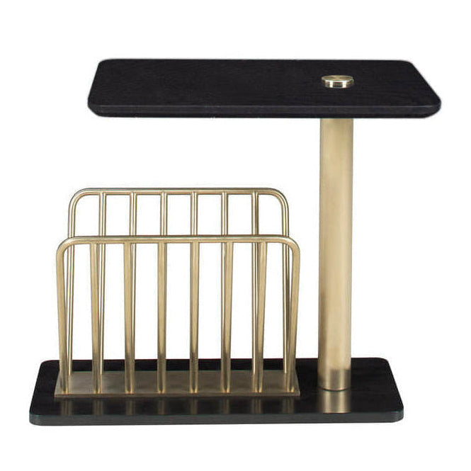 A modern side table with a black rectangular top and base, a central gold metal pedestal, and a gold wire magazine rack on a white background.