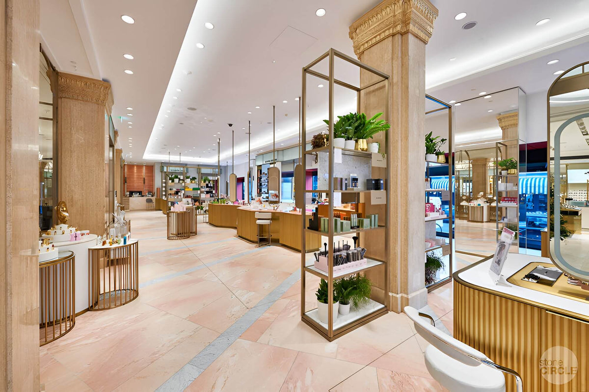 A luxury cosmetics store interior with marble floors, gold-framed display shelves, and modern retail fixtures under bright ceiling lighting.
