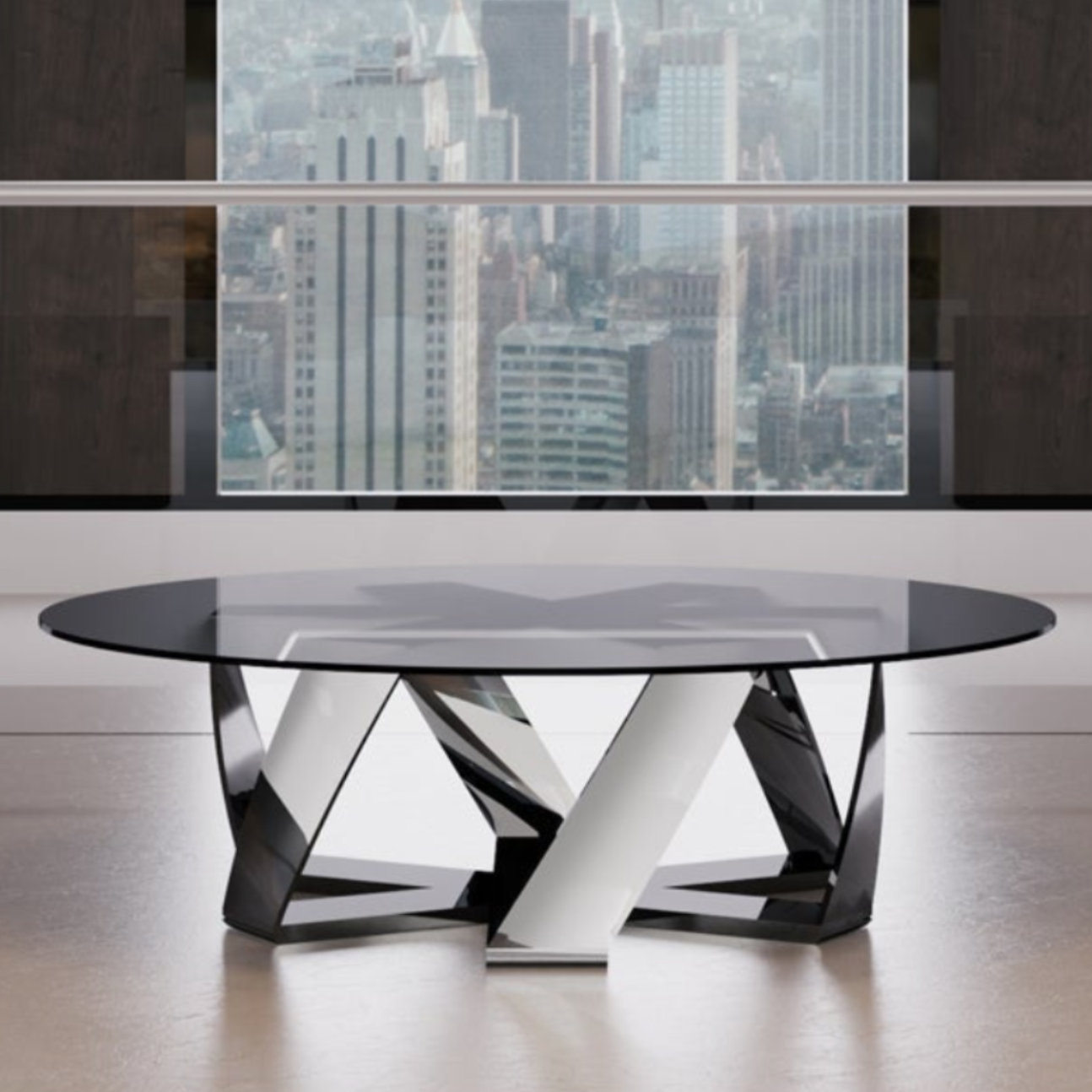 A modern round coffee table with a black glass top and a sculptural chrome and black metal base, positioned in a contemporary living room setting between two black armchairs with silver legs, set against a large window overlooking a city skyline.