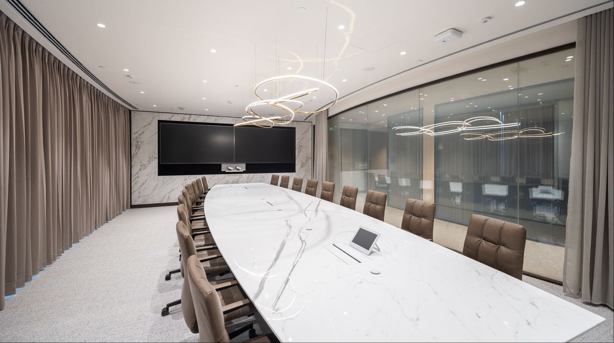 A modern conference room with a long white marble oval table, brown leather chairs, a large black wall-mounted screen, and a decorative spiral chandelier hanging from the ceiling.