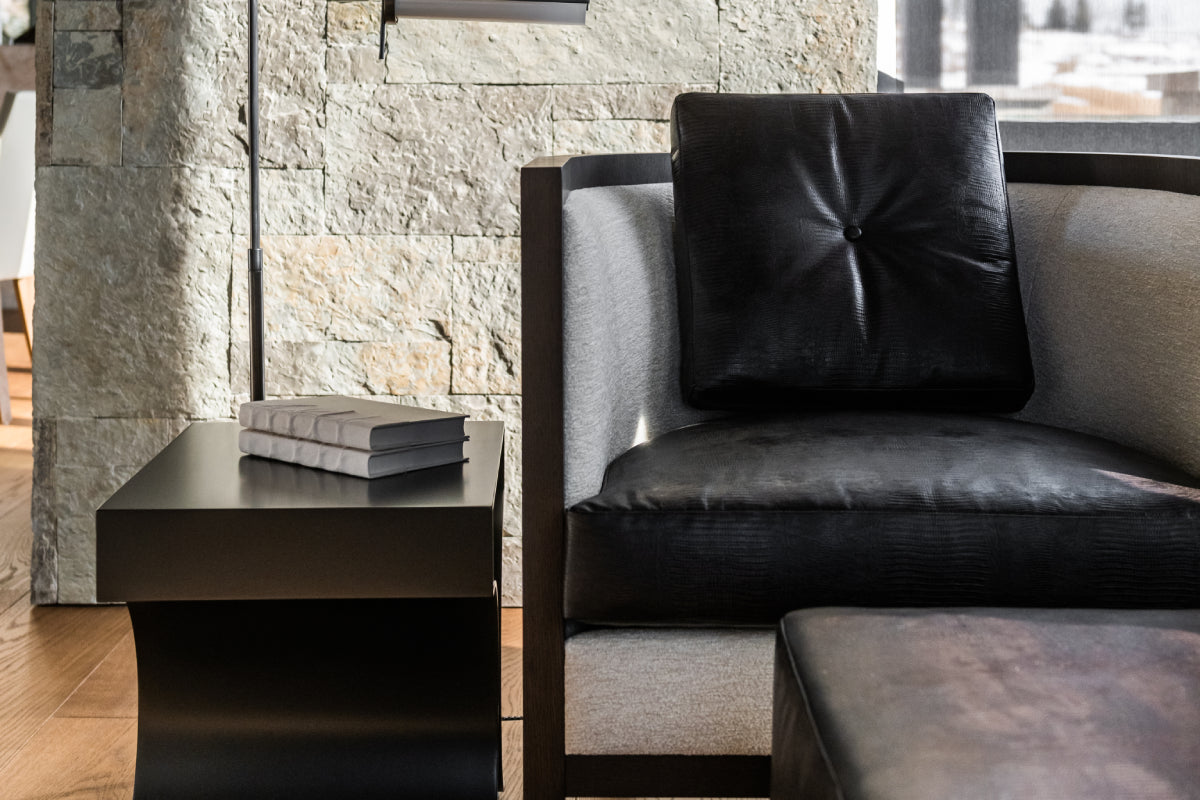 A modern black leather armchair with a tufted back cushion and light gray fabric sides, shown in a styled interior next to a black side table.