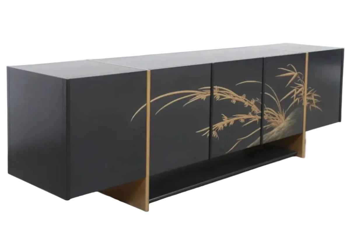 A modern black sideboard cabinet with gold bamboo and grass motifs painted on the doors, supported by gold-colored geometric legs, set against a white paneled wall and concrete floor.