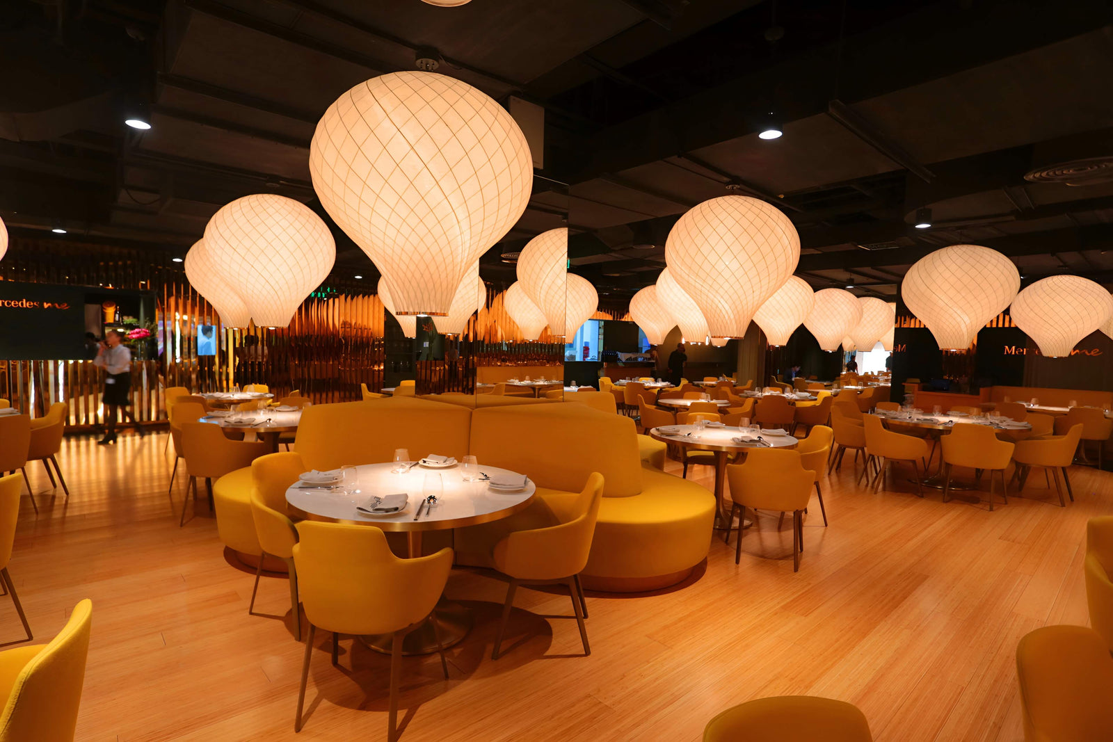 Modern restaurant interior with yellow chairs and large round lights.