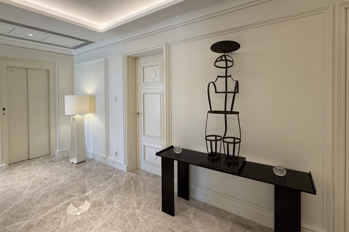 A modern black console table in a bright, elegant hallway featuring cream paneled walls, marble flooring, and a black wireframe decorative sculpture.