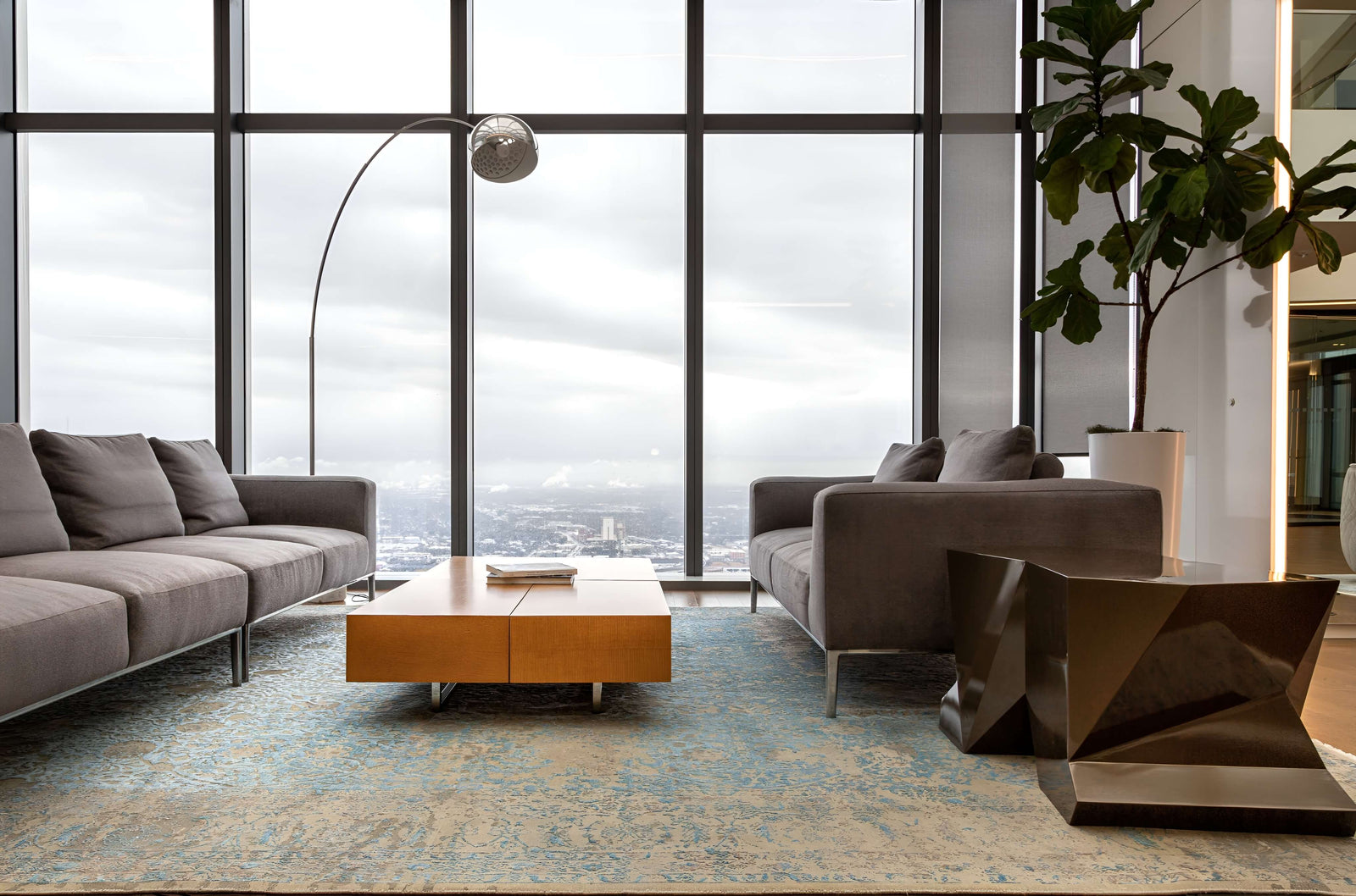 Modern office space with large windows, gray sofas, and a wooden coffee table.