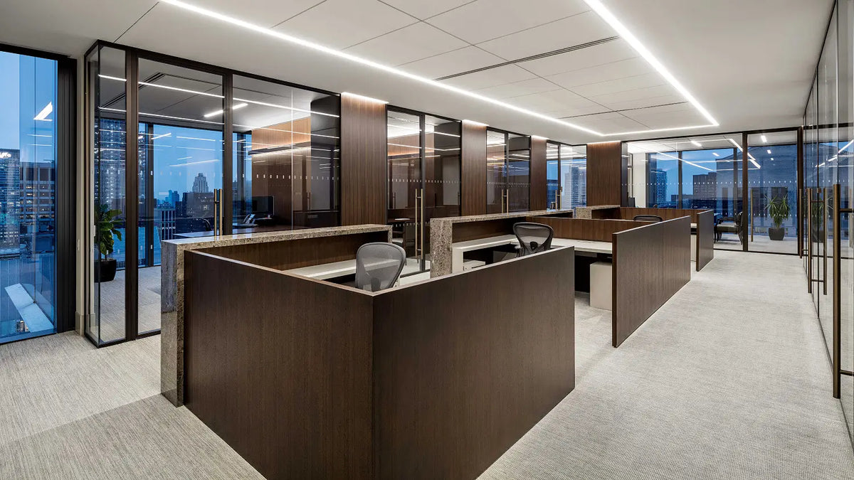 Modern open-plan office interior with dark wood cubicle dividers, glass walls, office chairs, and a light gray carpeted floor.