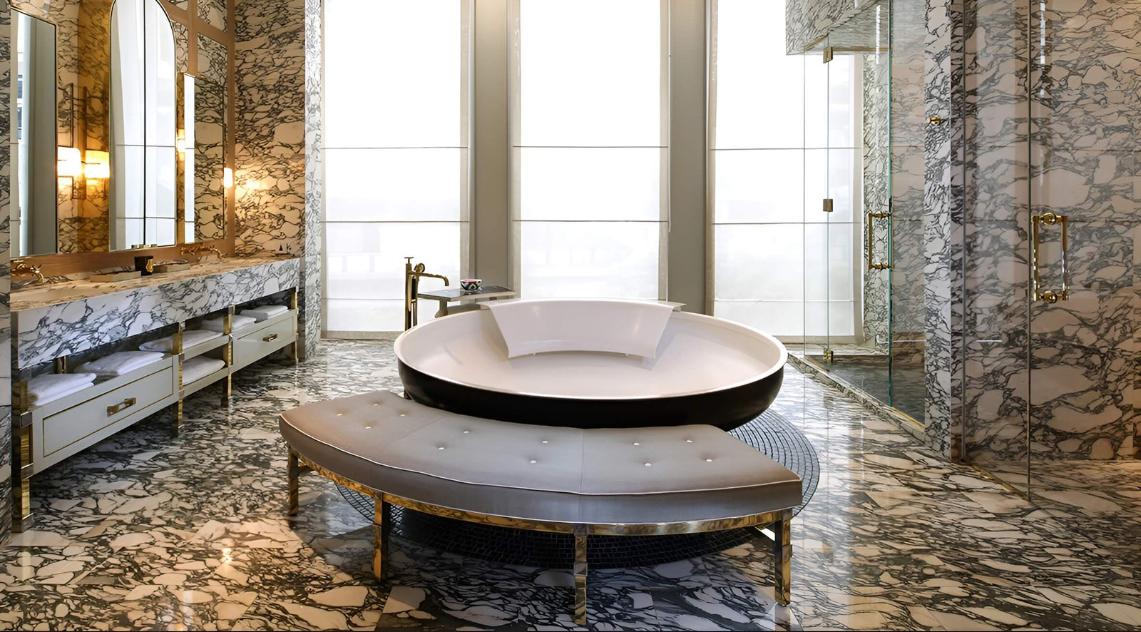 Modern bathroom with marble walls and floor, round white bathtub, and bench.