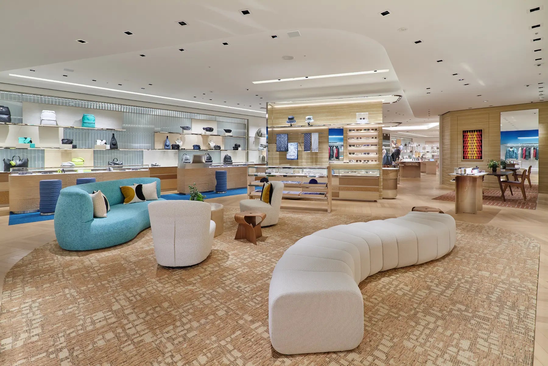 A spacious, modern retail interior with curved upholstered seating in white and turquoise, display shelves, and warm wood-toned fixtures on a patterned beige carpet.
