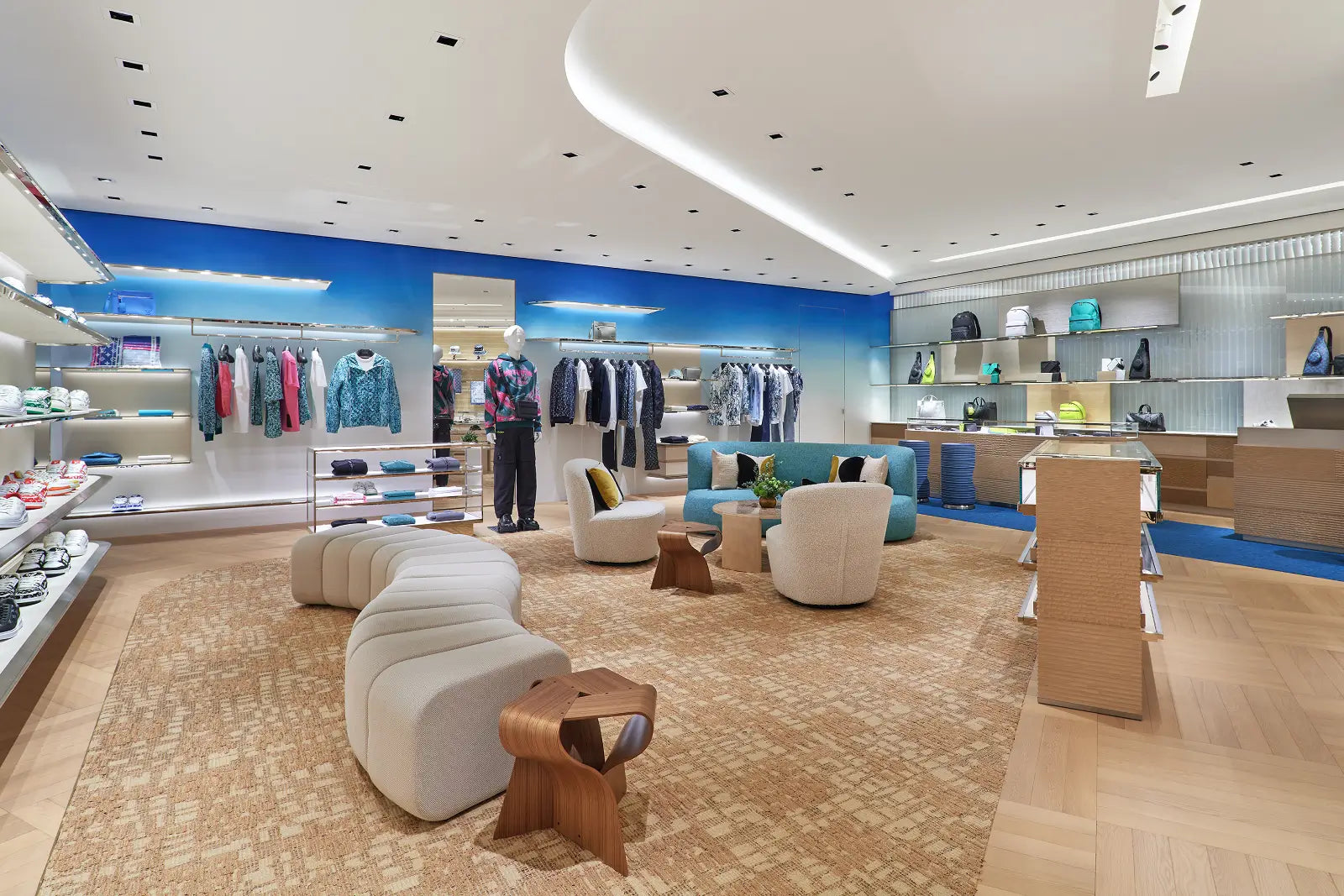 A spacious retail store interior with curved white seating, clothing racks, shelves, and a blue accent wall under recessed lighting.