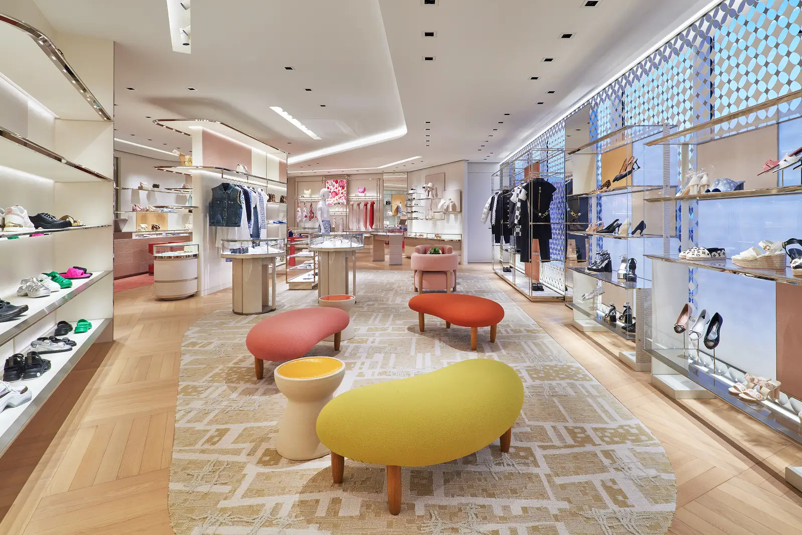 A spacious, modern shoe and apparel boutique with light wood flooring, white shelving, and colorful display stools in the center of the store.
