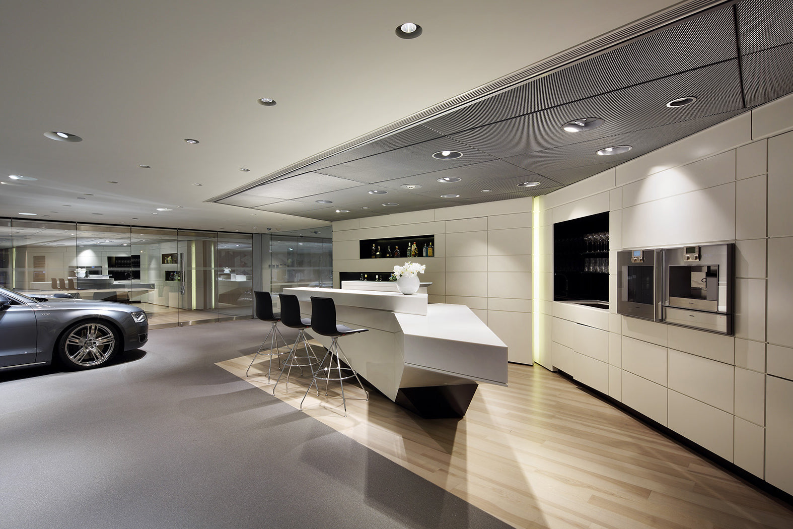 Modern showroom with white counter, bar stools and a car in the background.