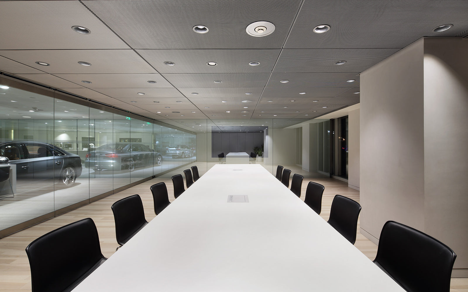 Modern showroom with a long white meeting table and black chairs with cars in the background.