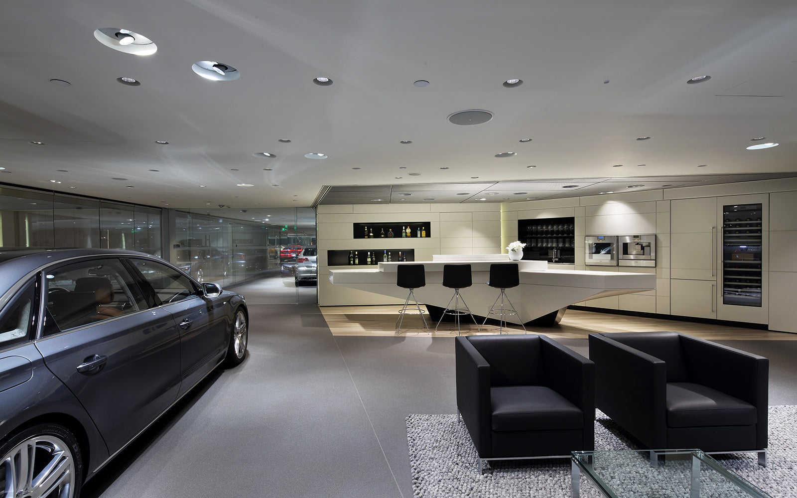 Modern car showroom with a gray car, black chairs, and a counter.