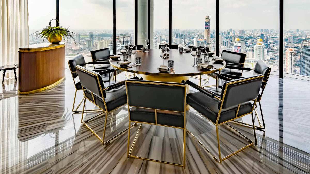 A luxury modern conference table set with black leather chairs featuring gold metal frames, positioned in a high-rise office with a panoramic city view.